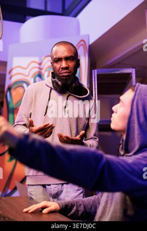 Hacker in hood pointing at illegal spyware code and asking developer for advice. Criminal showing crime partner malicious software on computer screen while cracking server password Stock Photo