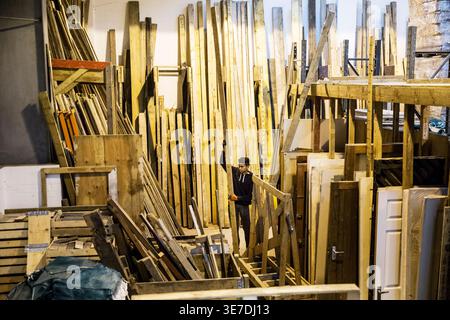 Mixed-race male teenager carpenter wearing gloves holding wooden plank while standing in workshop Stock Photo
