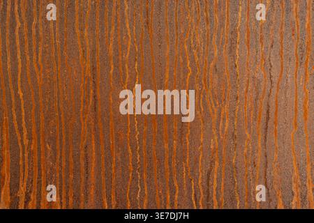 High-resolution close-up of a rusted metal surface featuring vertical orange-brown corrosion streaks. The weathered, oxidized texture creates a raw in Stock Photo