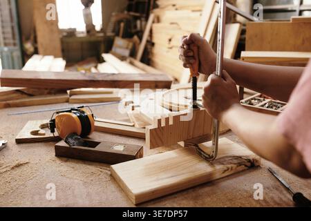 Cropped image of Asian female carpenter hands gluing and joining wooden furniture parts with clamps working in workshop Stock Photo