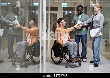 Black man looking at white coworkers shaking hands while standing in office hallway Stock Photo