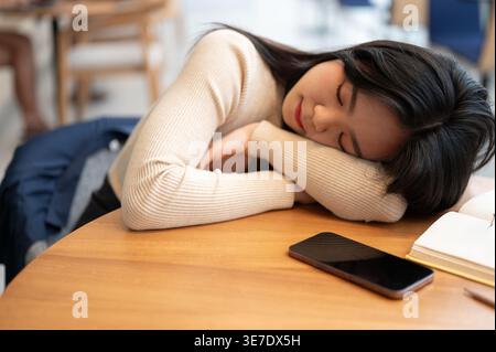 Sleeping Asian woman leaning on table with smartphone sitting in cafe Stock Photo