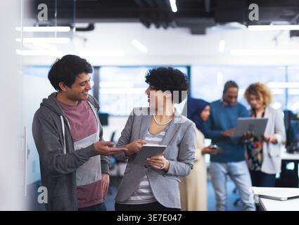 Smiling Mixed race man and woman looking at each other standing in office Stock Photo