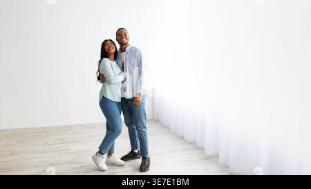 Smiling Black couple embracing and looking away while standing at home Stock Photo