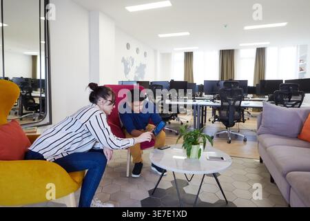 Middle Eastern male watching on tablet with caucasian female coworker sitting on sofa in office relaxation area during break Stock Photo