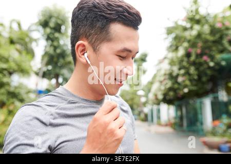 Portrait of smiling young Asian fit man wearing earbuds and making hands free phone call to his friend or coach Stock Photo