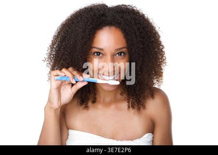 Smiling Black woman with afro brushing teeth standing against white background Stock Photo