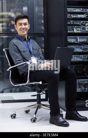 Chinese male technician using laptop sitting on chair in computer room Stock Photo