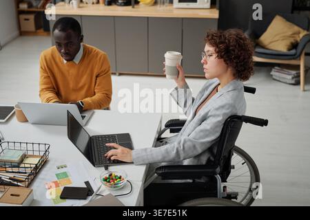Black man working with disabled caucasian female colleague using laptop sitting at table in office Stock Photo