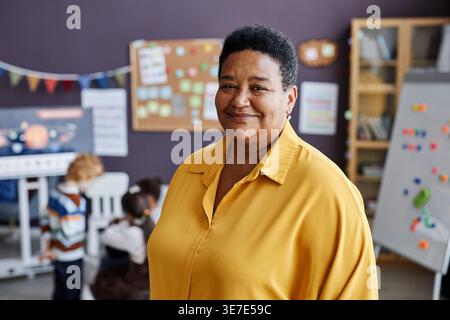 Middle-aged Black female teacher standing near her students in nursery classroom Stock Photo