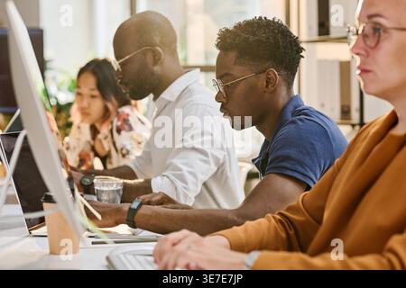 Diverse group of programmers working together while sitting at desk in office Stock Photo