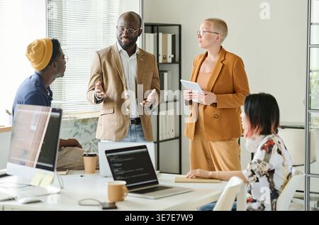 Diverse group of programmers discussing new project while standing in office Stock Photo