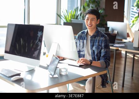 Chinese male college student using computer sitting at table in computer room Stock Photo