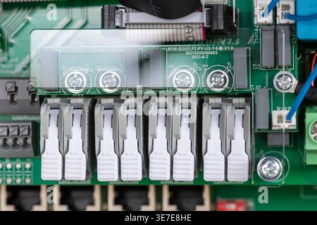 High-resolution macro image of a green printed circuit board (PCB) featuring multiple white connectors, terminal screws, and wiring components. Stock Photo