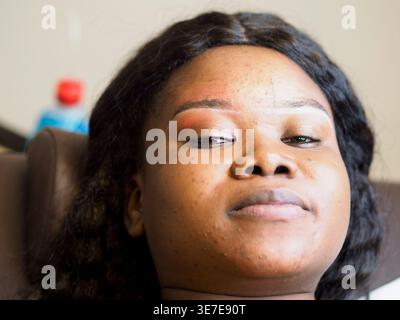 Black female client with white dye on her eyebrows waiting for threading while sitting in salon Stock Photo