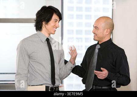 Mixed race and Chinese businessmen talking standing near window in office Stock Photo