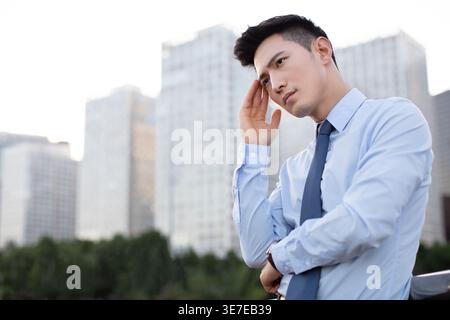 Chinese businessman having headache standing on bridge in city at sunset Stock Photo