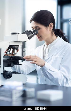 Chinese female scientist looking through microscope while working in laboratory Stock Photo