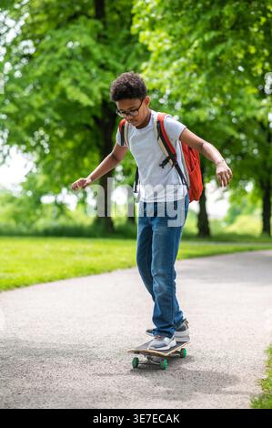 Black pre-teen boy wearing eyeglasses riding skateboard while in park Stock Photo