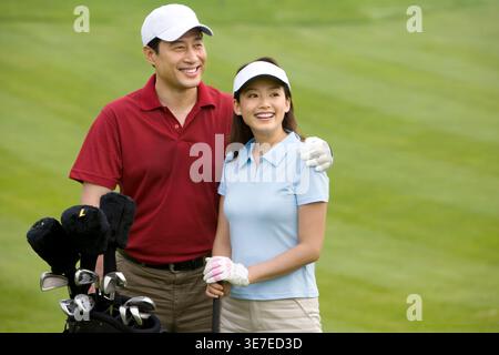 Smiling Chinese couple playing golf while standing on golf course Stock Photo