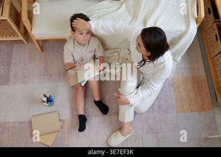 Asian mother teaching her Mixed race son homework for school sitting in living room at home Stock Photo