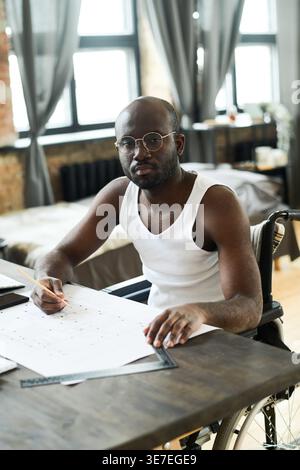 Disabled Black architect in eyeglasses sitting at table and concentrating on his work at home Stock Photo