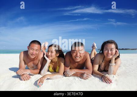 Smiling Chinese friends lying down together on sand on beach during daytime Stock Photo
