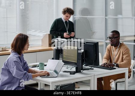 Group of diverse developers sitting at desk writing codes for new computer program in IT office Stock Photo