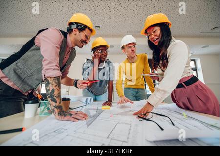 Close-up shot Diverse group of architects wearing safety helmets busy working with blueprints on the table in the office Stock Photo