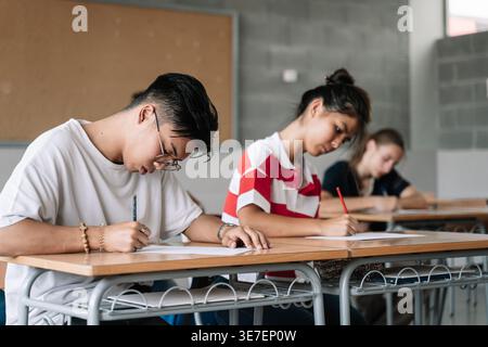 Asian male student and classmates sitting at desk taking exam in classroom Stock Photo