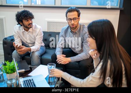 Serious diverse group of business people sitting on couch near table with laptop having a meeting in the office Stock Photo