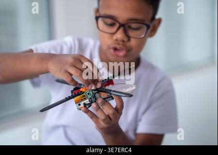 Serious Black boy in eyeglasses playing helicopter toy while sitting on floor at home Stock Photo