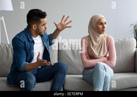 Middle Eastern man yelling at his irritated girlfriend while sitting on sofa at home Stock Photo