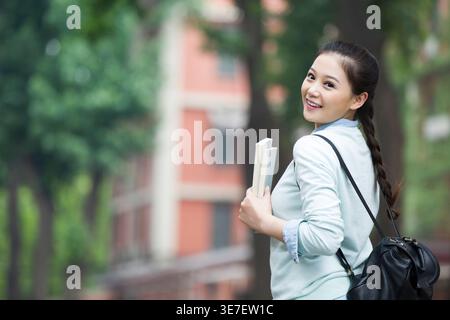 Chinese female college student looking over shoulder standing near school building Stock Photo
