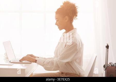 Smiling Black business woman with curly hair working on laptop in office during daytime Stock Photo