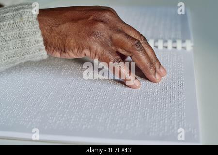Hand of Black man reading braille at table at home Stock Photo
