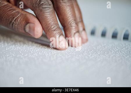 Hand of Black man reading braille at table at home Stock Photo