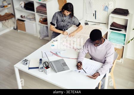 Diverse group of male and female tailors working together while sitting at table in atelier Stock Photo