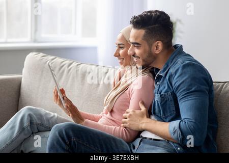 Smiling Middle Eastern couple using tablet while sitting on sofa at home Stock Photo