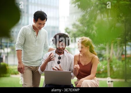 Black businessman gesturing hands looking at laptop screen discussing project details with Asian male and caucasian female colleagues sitting in ci... Stock Photo
