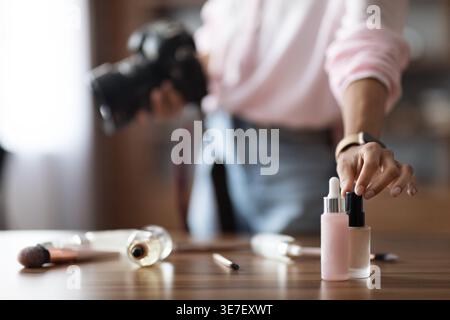 Cropped image of Middle Eastern woman holding camera touching cosmetics while standing at table in office Stock Photo