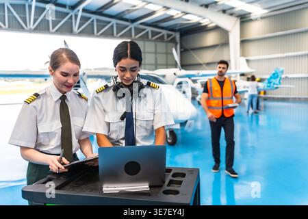 Middle Eastern female pilot using laptop standing beside her co-pilot preparing for flight in hangar Stock Photo