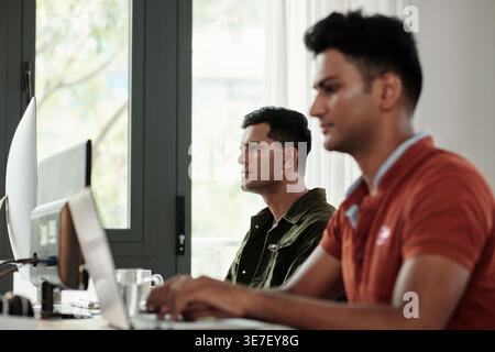 Serious Indian businessmen working on computers together sitting at table in office Stock Photo