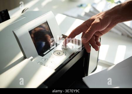 Hands of Mixed race man pressing button on printer to print documents in office Stock Photo