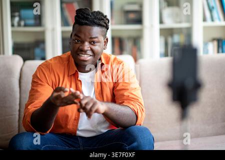 Black man with braids doing live-streaming sitting on sofa in living room at home Stock Photo
