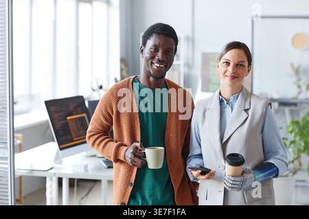 Black male programmer holding coffee cup standing beside disabled female colleague with bionic arm in office Stock Photo