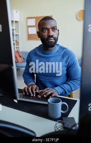 Black male programmer with beard  typing codes on computer while sitting at table in office Stock Photo