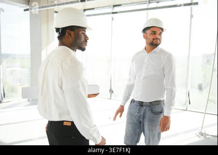 Diverse group of male engineers wearing hard hats walking together and doing inspection on construction site Stock Photo