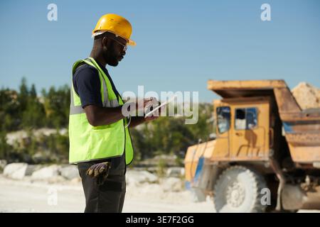 Black male engineer wearing safety helmet and sunglasses using tablet while standing in construction site Stock Photo
