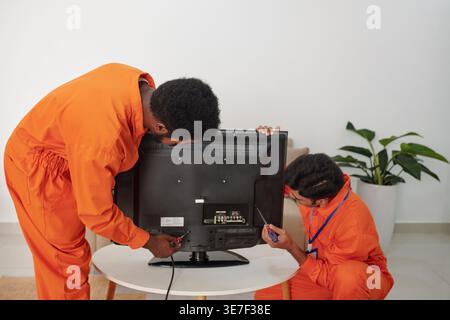 Diverse group of male technicians in orange suit putting television set on coffee table and plugging it in costumer's home Stock Photo